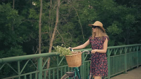 Woman In Hat. Girl In Sunglasses. Attractive Girl Walking With Bicycle On The Bridge. Wicker Basket.