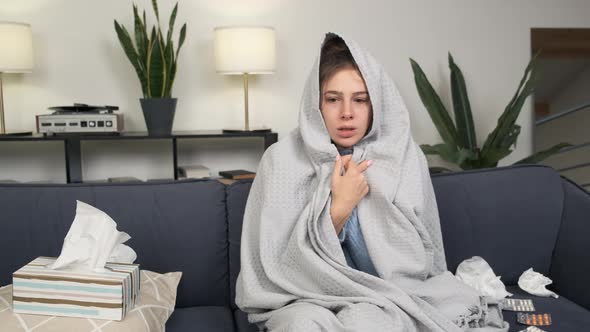 Young Unsatisfied Sick Woman Covered with Warm Blanket Plaid Sitting Alone on Couch in Living Room