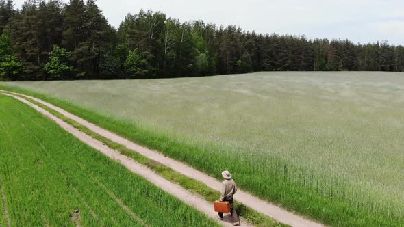 Man Alone Walking By Country Road in a Green Field, Holding Suitcase in a Hand, Funny Travel Concept