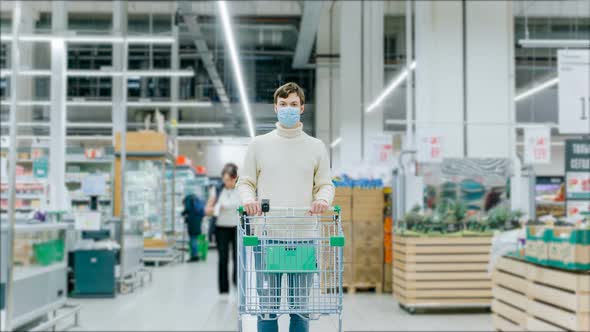 A Man in a Medical Mask Stands with a Grocery Cart in a Supermarket, Timelapse. Protection From