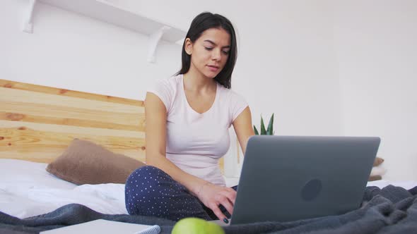 Сheerful Young Woman Working at Home Using Laptop in Bed in the Morning