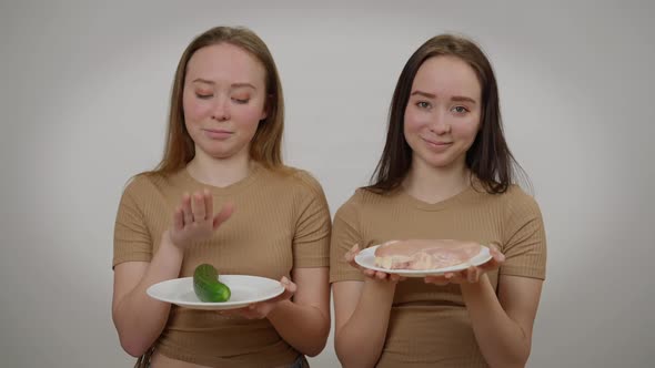 Twin Sisters Posing with Raw Meat and Fresh Organic Cucumber at Grey Background