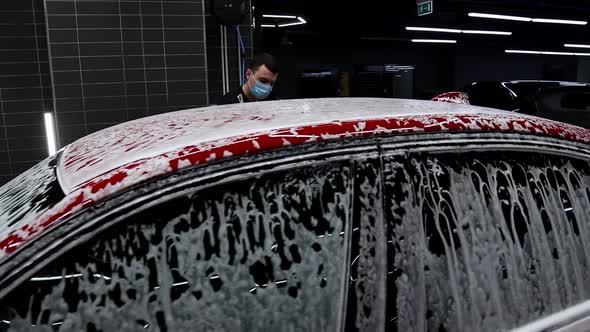 Man Washes Car Covered with Foam in the Car Washing Salon