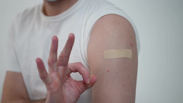 Closeup Male Hand Gesturing OK at Shoulder with Medical Patch After Covid19 Vaccination