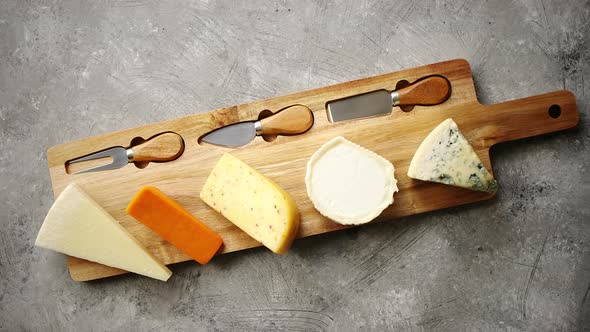 Assortment of Various Kinds of Cheeses Served on Wooden Board with Fork and Knives