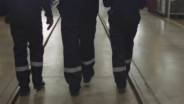 Rear View Of Plant Workers In Coveralls Walking Through Mill