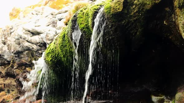 Small coastal waterfall landing on green mossy rocks, tilt-down shot