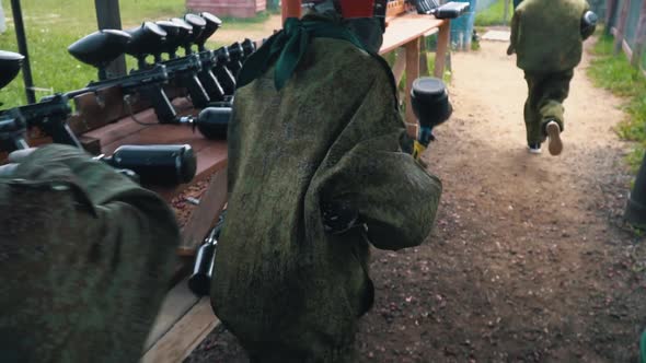 Paintball Players in Camouflage Uniforms Take Guns and Run