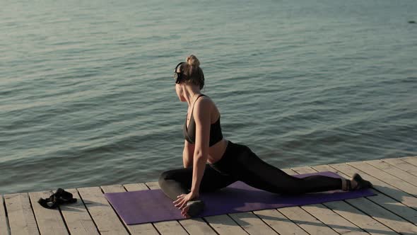 Woman Is Practicing Yoga Stretching Legs and Tilting Ahead on Mat on River Pier.