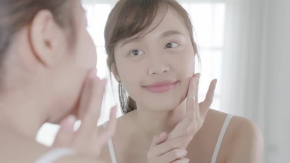 Beautiful young asian woman happy applying cream or lotion with moisturizer to skin face.