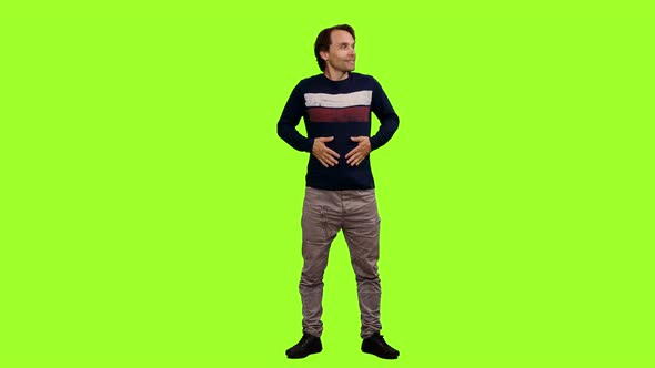 Elegant Man Stands with Hands in Pockets on Green Background