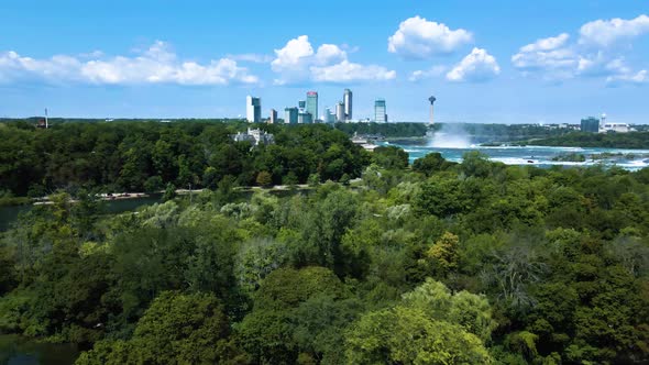 Aerial backwards shot of Niagara Falls, skyscraper skyline and rural forest with trees on canadian b