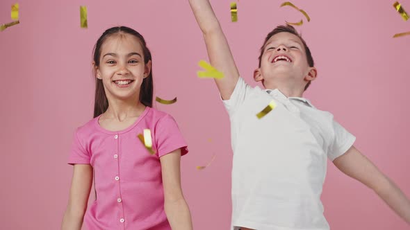 Studio Portrait of Happy Little Boy and Girl Throwing Golden Glitter Up and Enjoying Rain Dancing