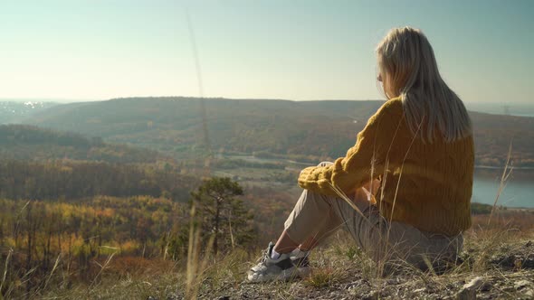 Young woman sits on the stones and enjoys autumn forest in the mountains