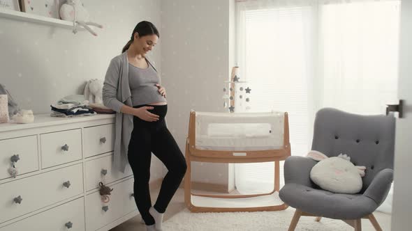 Caucasian woman in advanced pregnancy standing in the baby's room next to the crib.