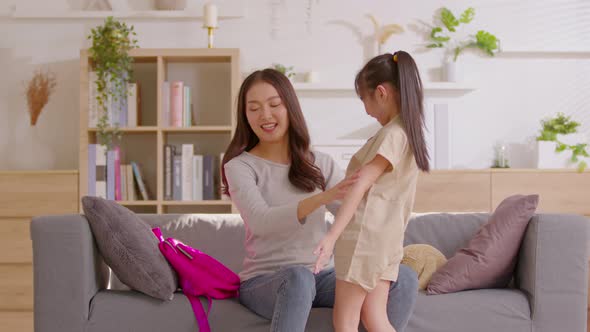 Mom is checking her daughter's outfit and give her child a magenta back pack for carry on her back