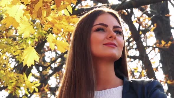 Young Beautiful Woman Looks Around in the Park in Autumn Day 
