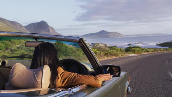 African american woman driving along country road in convertible car