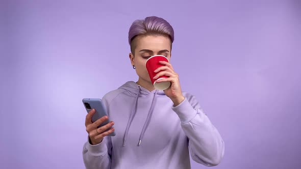 Mod Young Woman Using Phone Drinking Coffee Isolated Purple Background