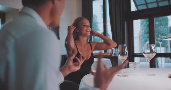 Woman playfully fixes hair while at the table with man