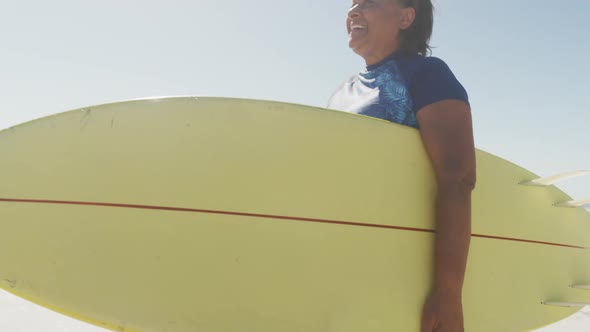 Happy senior african american woman walking with surfboard on sunny beach