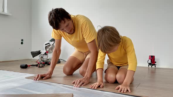 Father and His Little Son Install Laminate on the Floor in Their Apartment