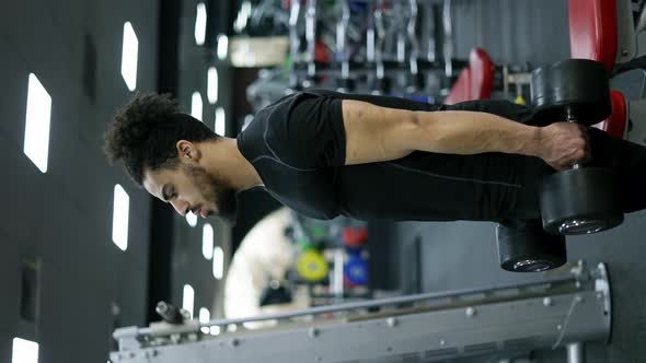 Muscular Man Uses Dumbbells to Exercise His Shoulders in Fitness Gym