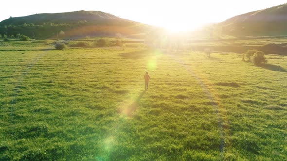 Flight Over Sport Man at Perfect Green Grass Meadow. Sunset in Mountain