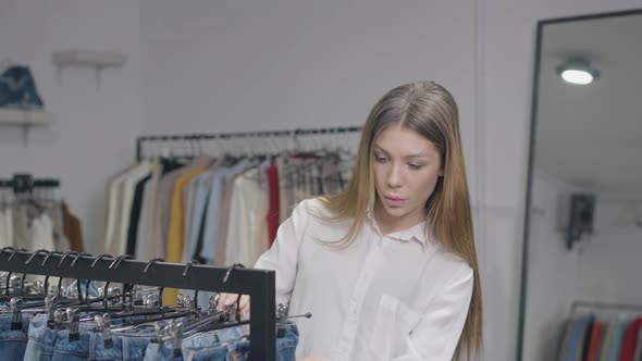 Portrait of Young Concentrated Woman Choosing Clothes in Shop Indoors