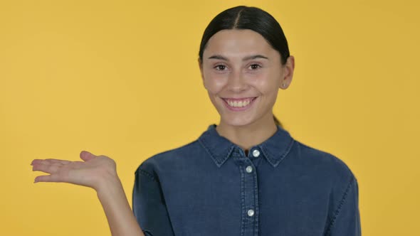 Latin Woman Holding Product on Palm, Yellow Background 