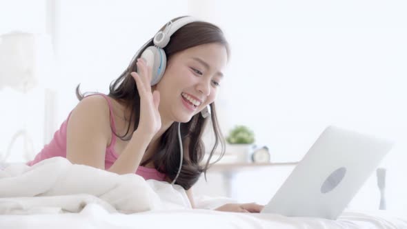 Beautiful young asia woman lying in bedroom using laptop computer relax listen music.