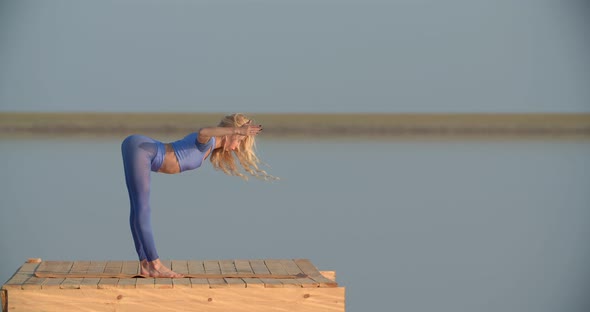 Blonde Woman in Blue Sportswear is Doing Yoga on a Platform in the Lake