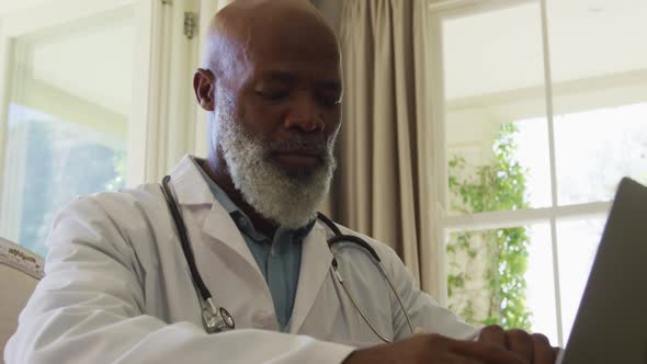 African american senior male doctor using laptop at home