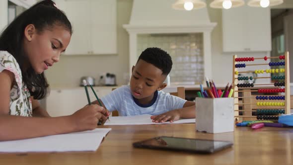 African american sister and brother sitting at kitchen table doing homework