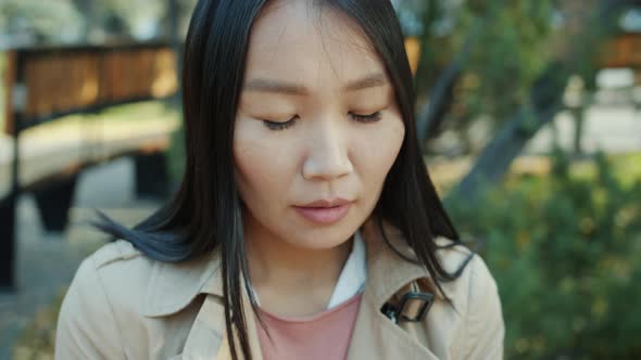 Closeup Portrait of Attractive Asian Brunette Touching Smartphone Screen Sitting Outdoors Alone