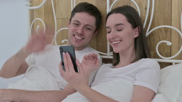 Young Couple Doing Video Chat on Smartphone in Bed