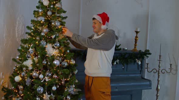 Man in Santa Hat Decorating Christmas Tree in Living Room