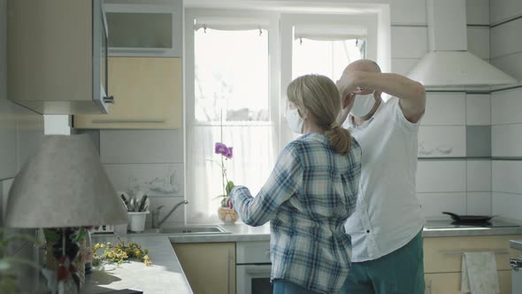 Man And Woman In Medical Masks Dancing In The Kitchen.