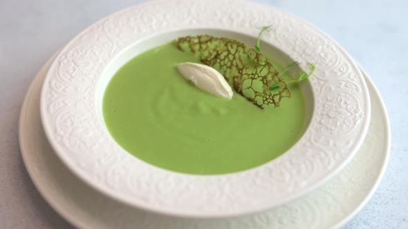 Woman's Hand Adorns Cheese Quenelle and Sprigs of Greens Homemade Soup Puree