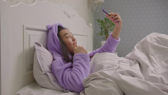 20s Asian Woman Talking Looking at Cell Phone Camera Lying in Bed