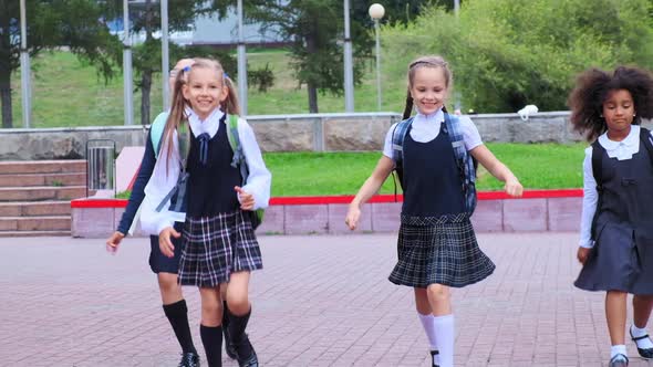 Cute Girls in Uniform Run Along School Yard Against Flowers