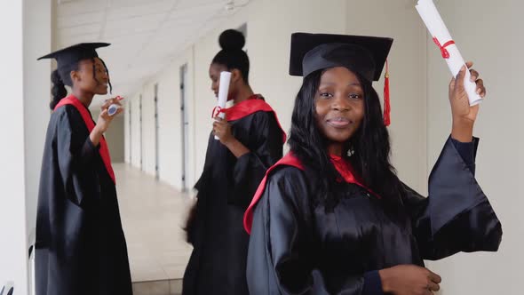 A Joyful Female Graduate with a Diploma in Hand Stands at the University Against the Background of