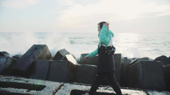 Attractive Young Woman in a Warm Jacket Walking on the Stone Beach at Sunset