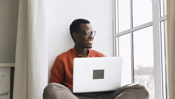 Happy AfricanAmerican Man with Laptop Looks Out of Window