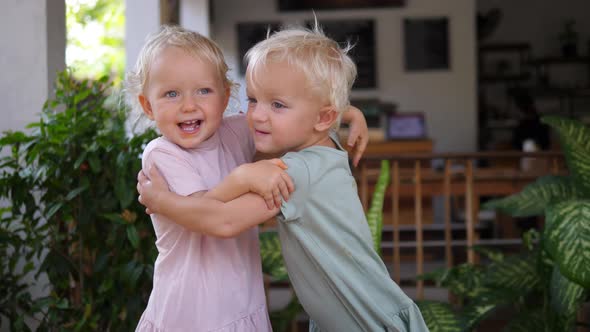 Two Blonde Small Sisters with Blue Eyes Expressing Family Love Cuddling and Smiling