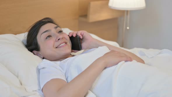 Young Indian Woman Talking on Phone while Sleeping in Bed