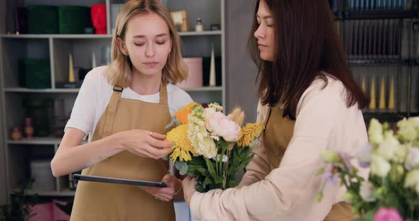 Women Florists Colleagues Standing in Flower Shop with Flowers, Using Digital Tablet