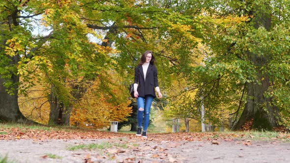 Teenage Girl Walking on Path in Public Park In Autumn Foliage Colors Slow Motion Low Angle Wide Shot