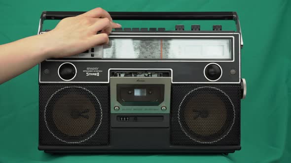 Girl Puts Vintage Cassettes Into a Black Radio Tape Recorder on Green Background