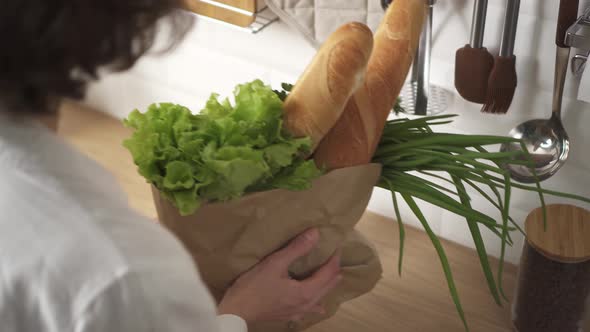 Young European Woman Brought Paper Eco Bag With Fresh Vegetables, Herbs, Baguette To Kitchen